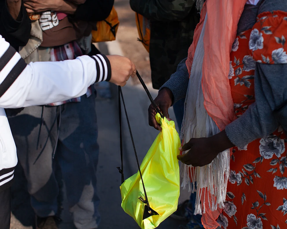 A close up of a volunteer handing an unhoused individual a bag of donated items by a West Valley Arizona community nonprofit
